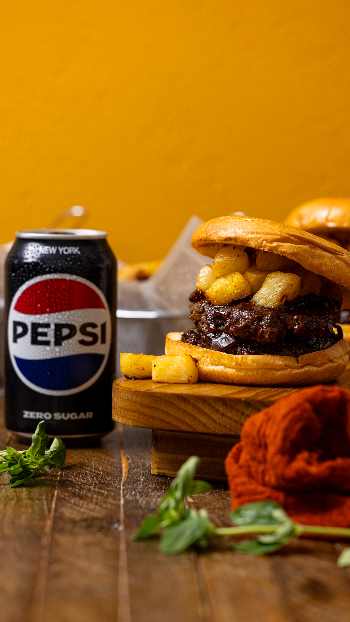 Photo of burger with Pepsi can on a brown wood table.