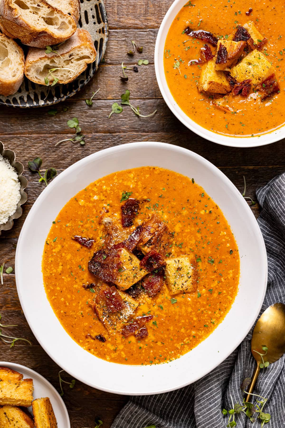 Photo of two bowls of tomato bisque on a wooden table with bread.